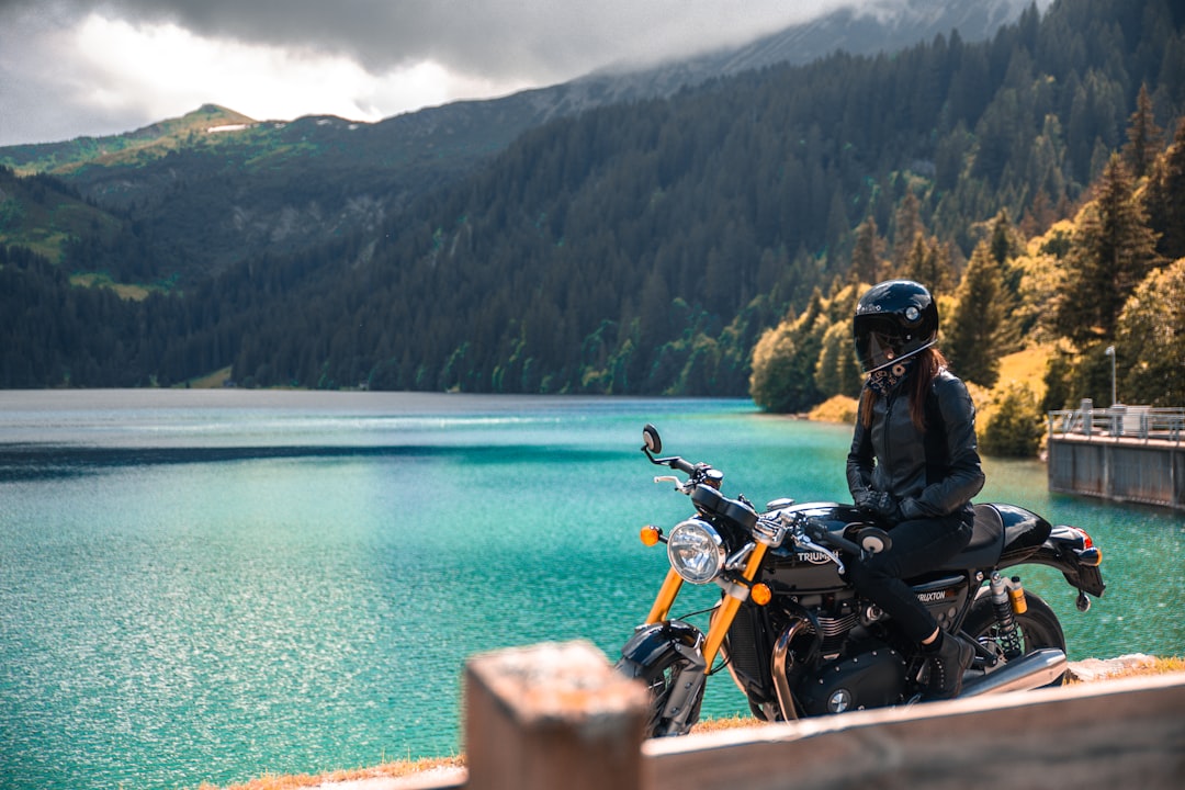 Man in black jacket riding motorcycle near body of water during daytime